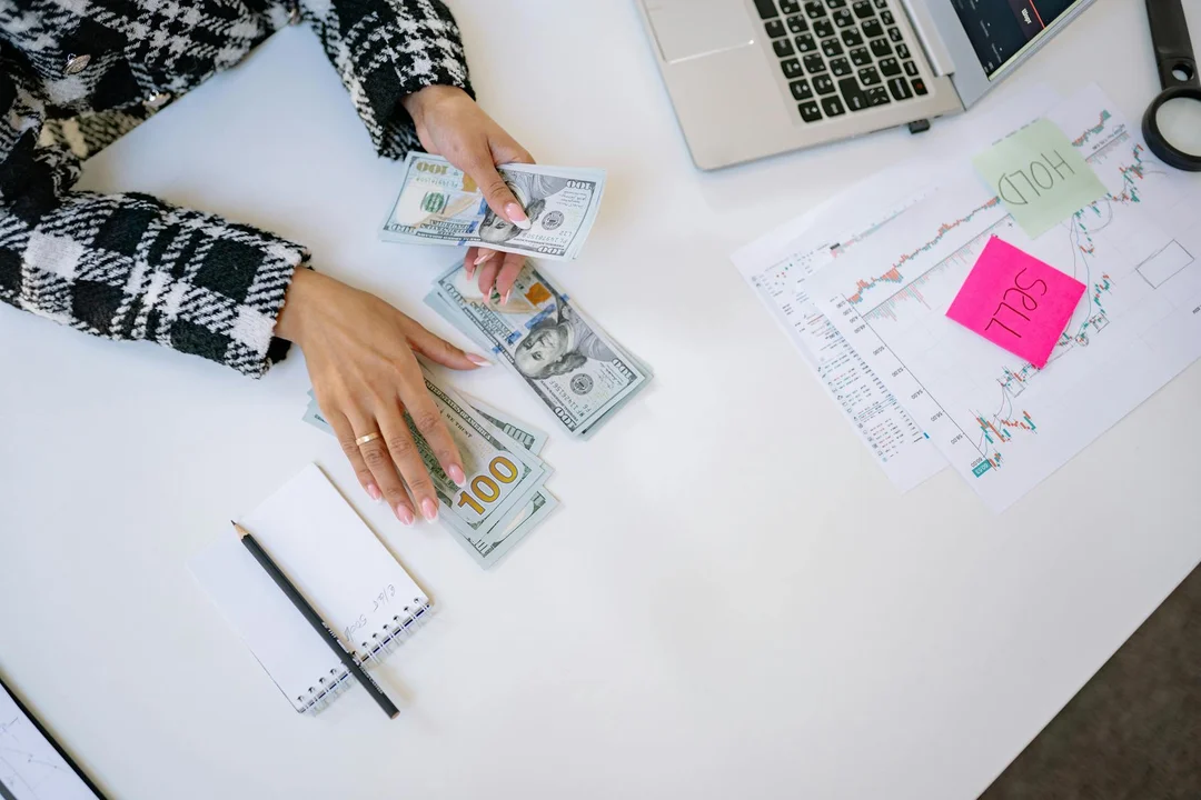 Person counting cash at a desk with a laptop and documents, symbolizing budgeting around HOA dues