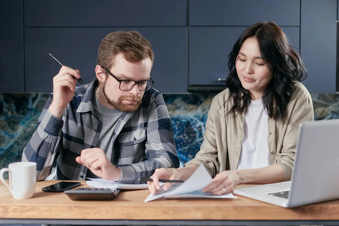 Two adults sit at a table reviewing documents and using a laptop to arrange HOA payments