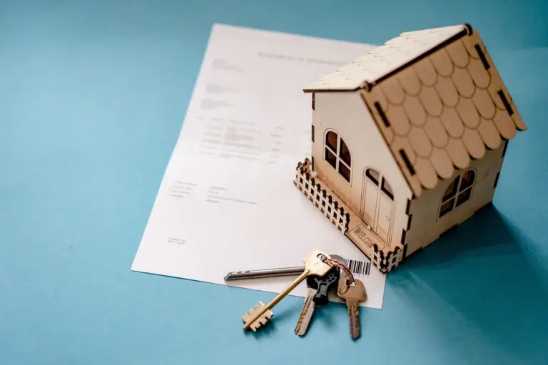 Small wooden house model with keys and a document on a blue background, symbolizing HOA insurance and ownership.