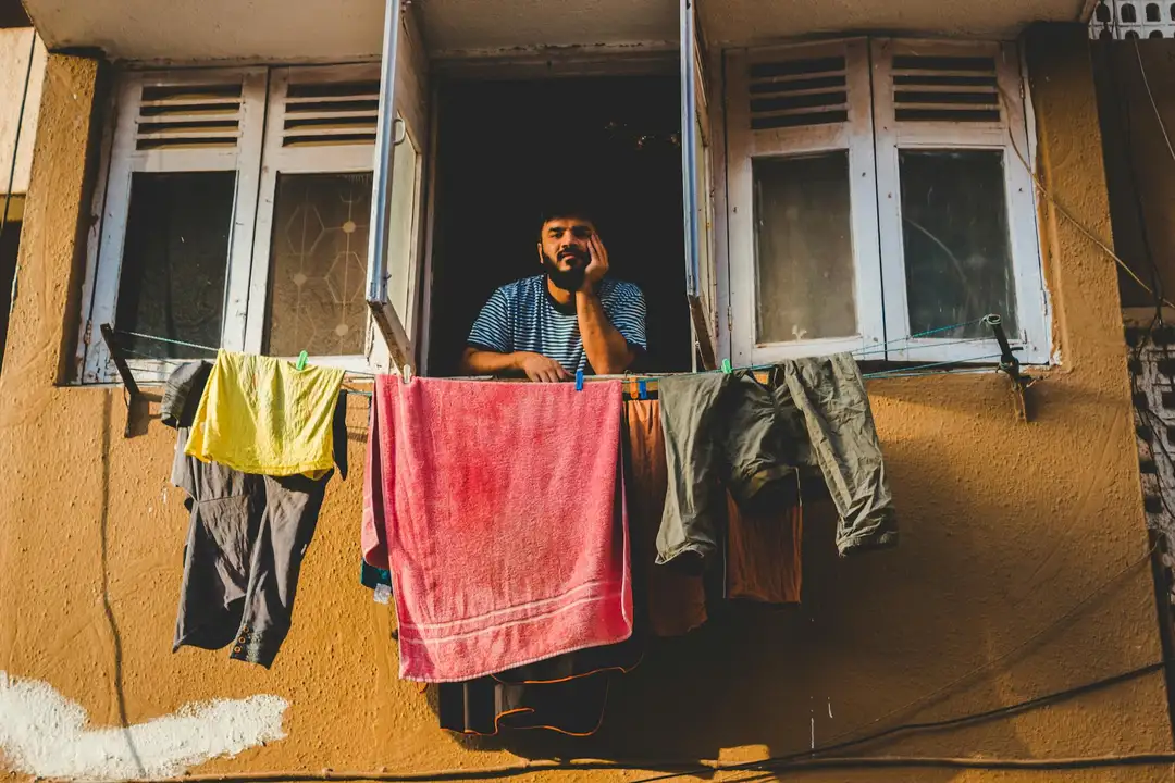 A resident leaning from an open window with clothes hanging to dry on an outdoor clothesline against a yellow building.
