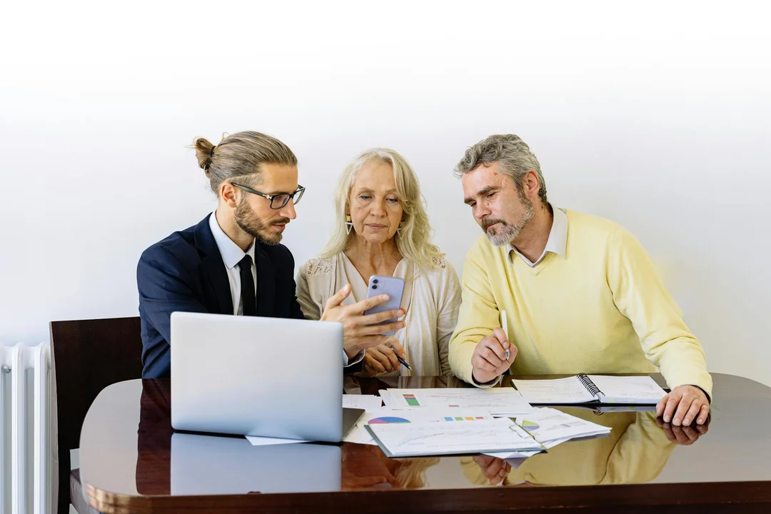 Three professionals seated at a conference table reviewing documents and a laptop during a planning session.