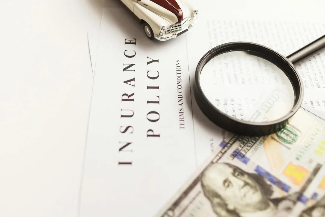 Close-up of an insurance policy document with a magnifying glass, a small model car, and scattered currency.