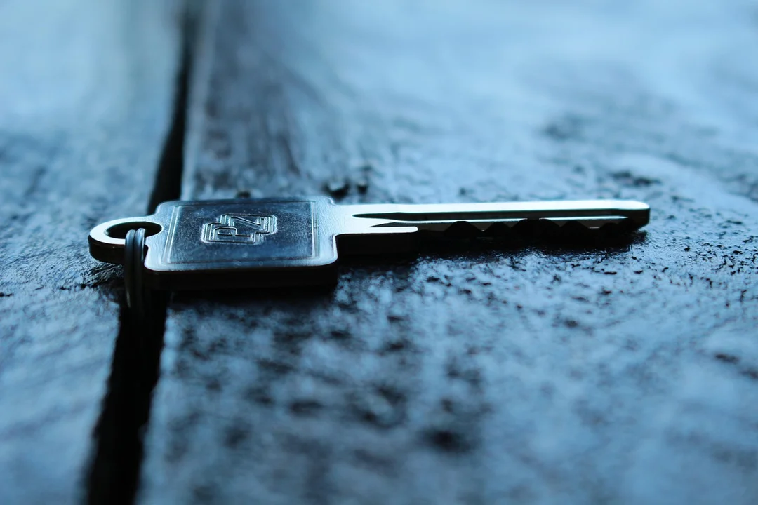 A single metal key lies on a rough, blue-toned wooden surface
