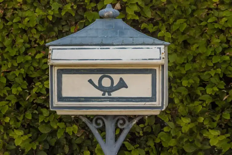 Blue and cream mailbox mounted on a metal post, surrounded by dense green ivy.