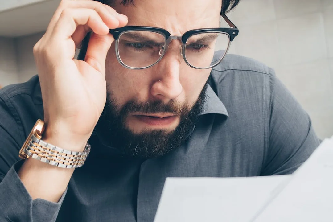 Close-up of a man with glasses examining a document, appearing thoughtful or concerned about HOA fees.