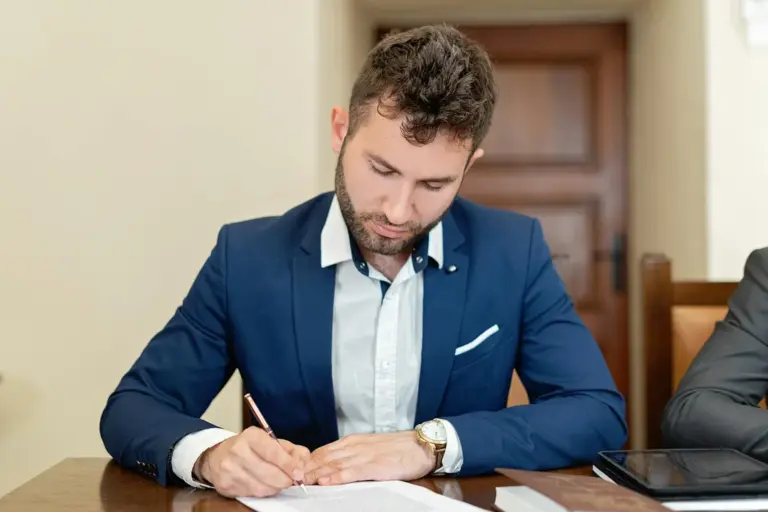 Man in a blue suit signing documents at a table