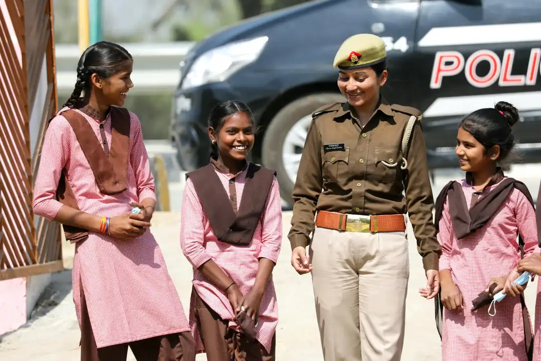 A police officer in uniform stands with three schoolgirls in pink uniforms outside, smiling and talking.