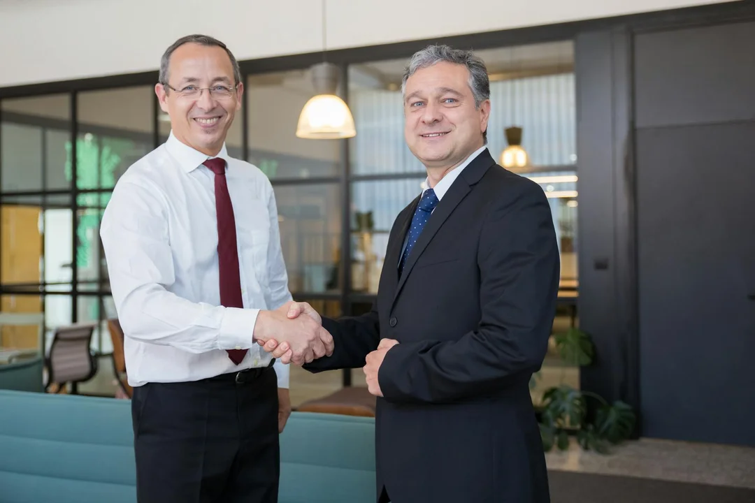 Two business professionals in a modern office shaking hands, illustrating a settlement reached through mediation.