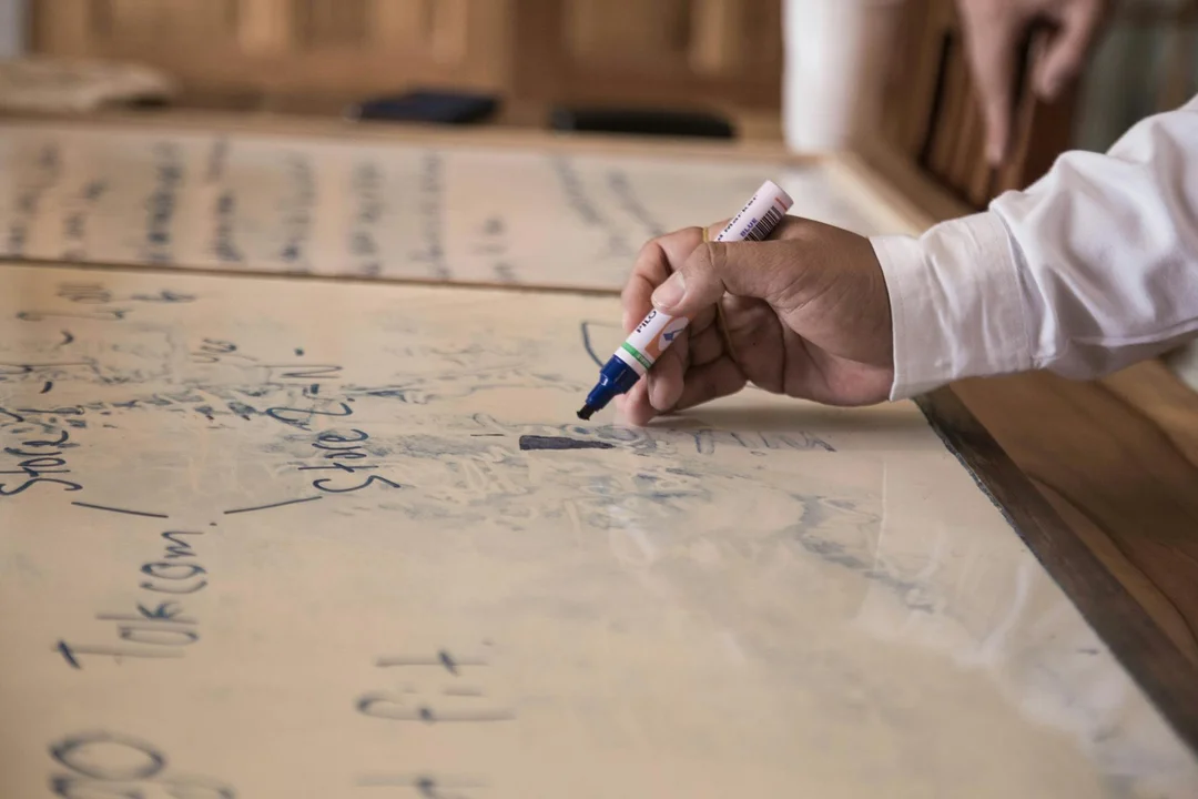 Close-up of a hand holding a marker writing on a large board during a mediation planning session.