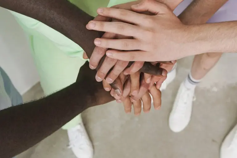 A diverse group of people placing their hands together in the center, symbolizing unity and mediation in HOA disputes.