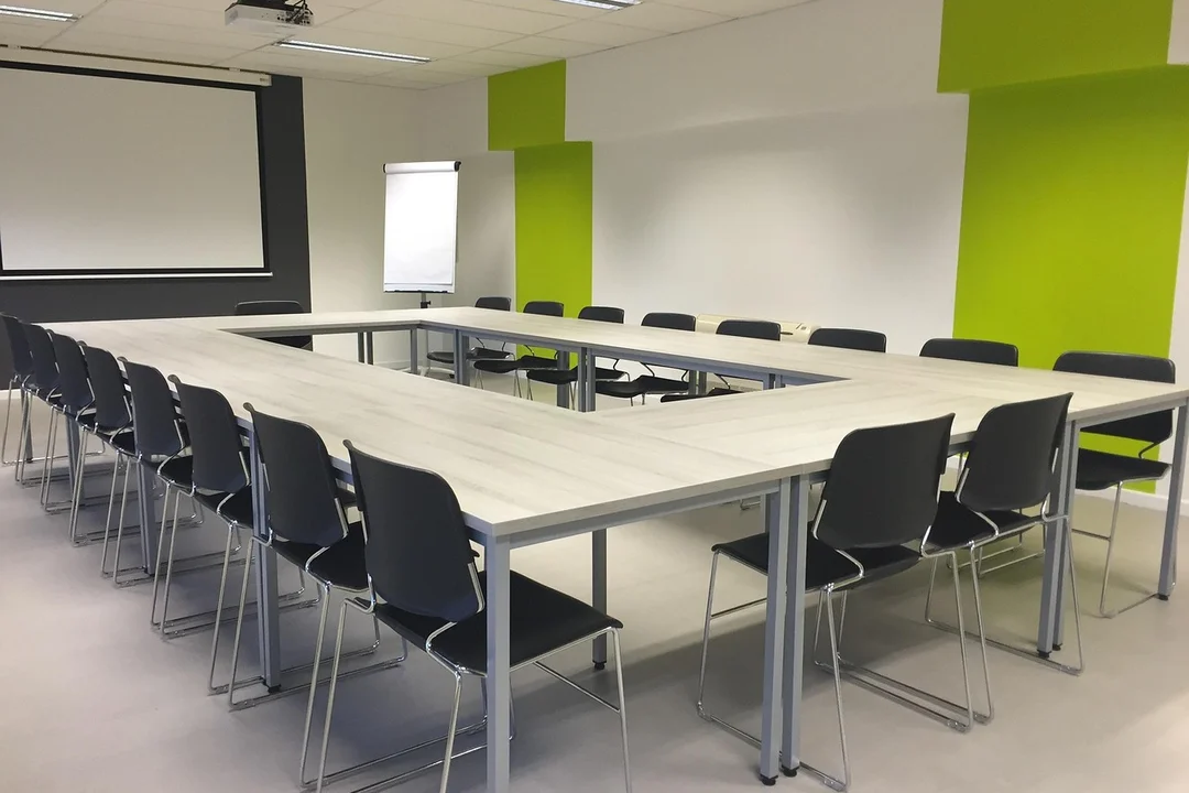A modern conference room with long U-shaped tables and black chairs around them, bright lime-green and white walls.