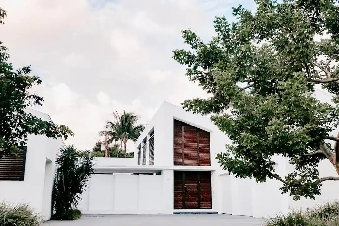 Modern white house with wooden shutters surrounded by trees.