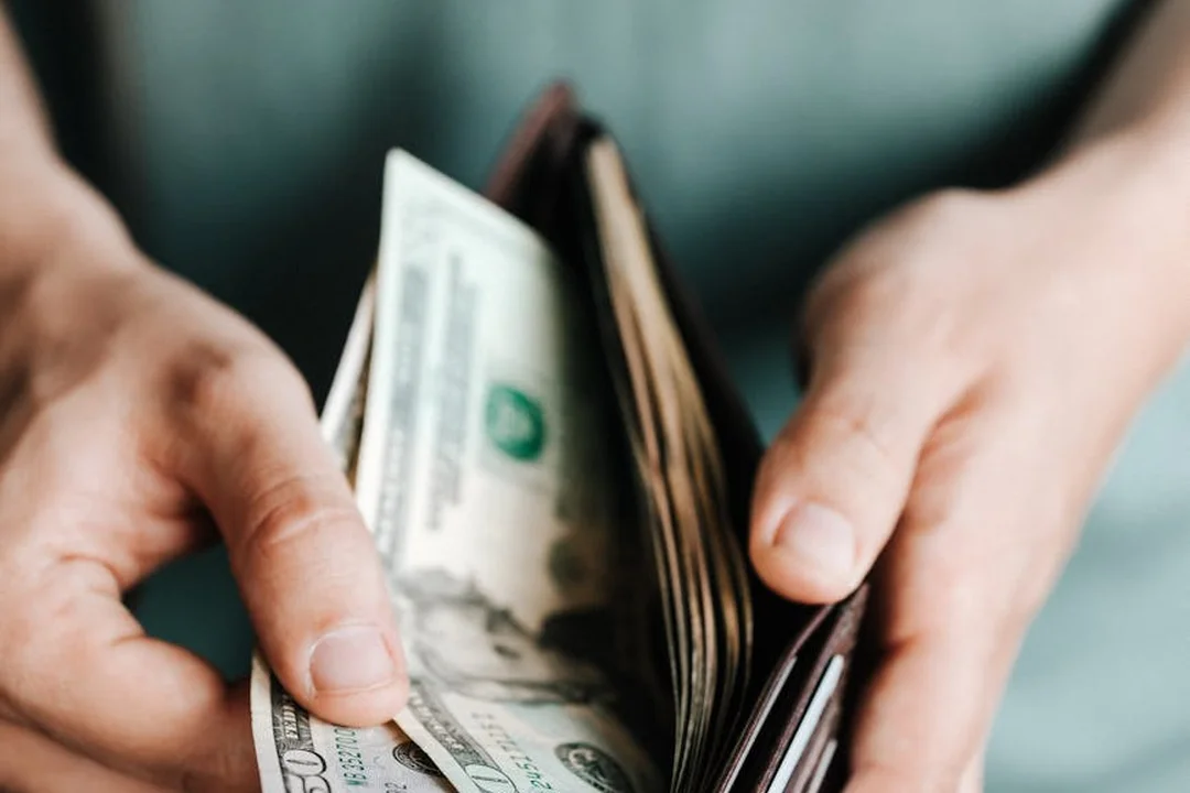 Close-up of hands holding cash and a wallet, symbolizing compensation and reimbursements for HOA board members