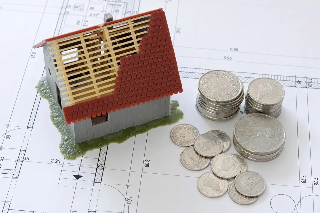 Miniature house model on architectural plans with stacks of coins, representing cost and legal steps.