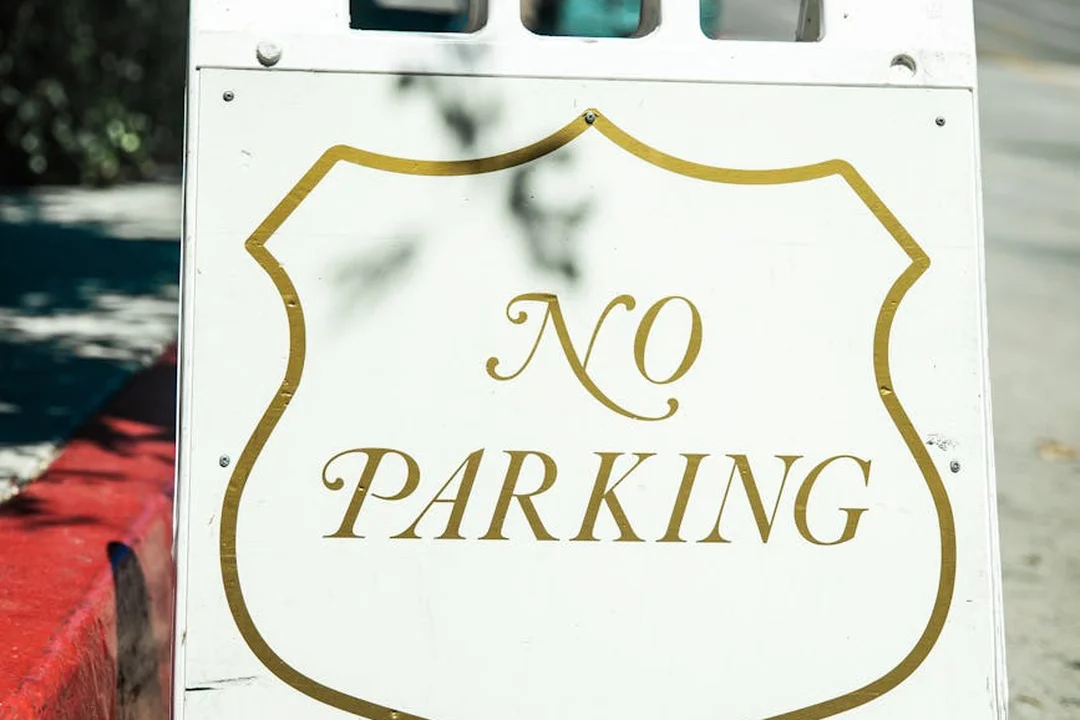 White sign with a gold-bordered shield reading 'NO PARKING'.