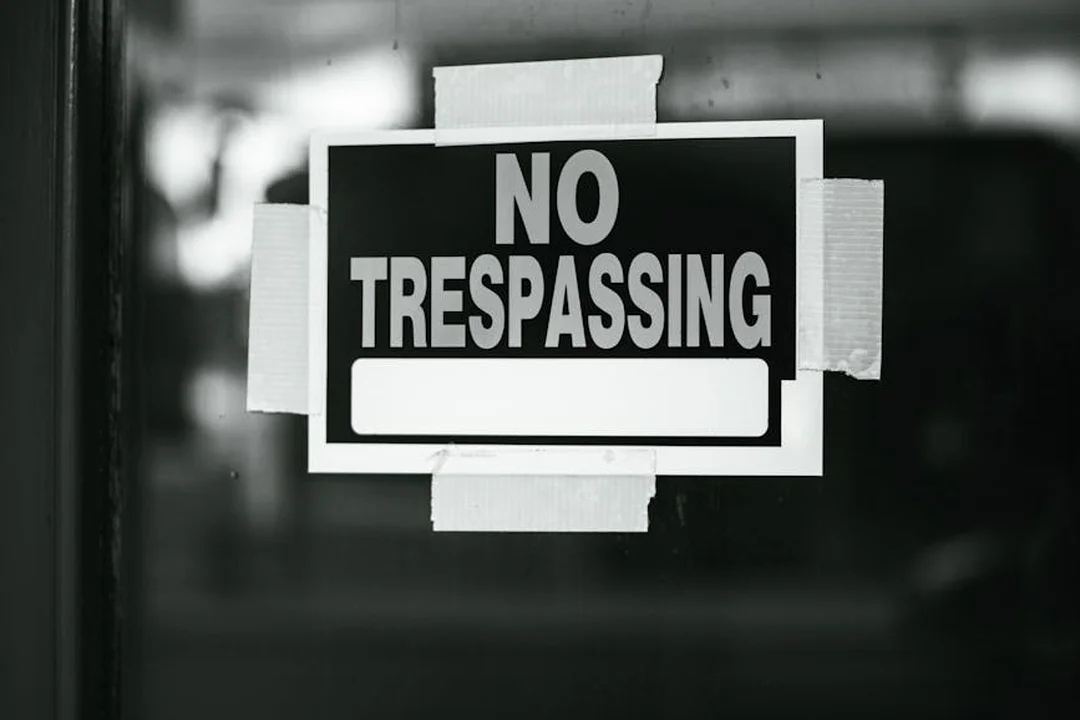 Black-and-white photograph of a 'NO TRESPASSING' sign taped to a glass door.