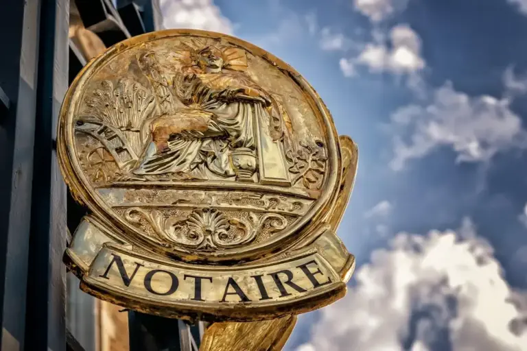 Close-up of a brass notary sign reading 'NOTAIRE' mounted on a building with a blue sky backdrop.