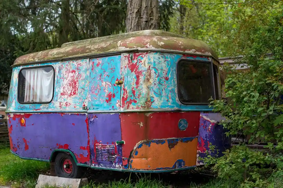 Colorful, weathered vintage trailer in a grassy, wooded lot