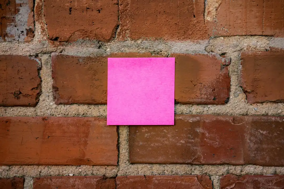 Bright pink sticky note on a textured red brick wall