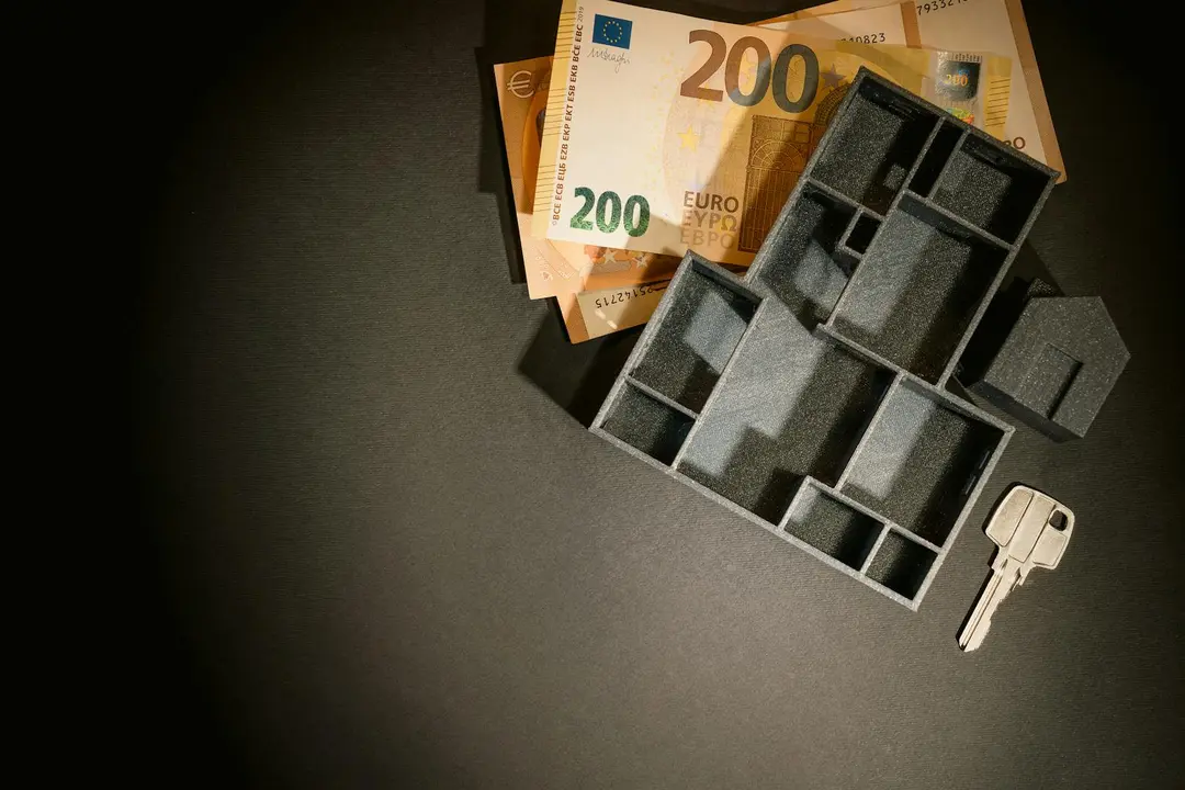 Architectural model of a house with scattered 200 euro banknotes and a key on a dark surface, representing transfer of ownership and ongoing asset management after a developer-to-homeowner transition.