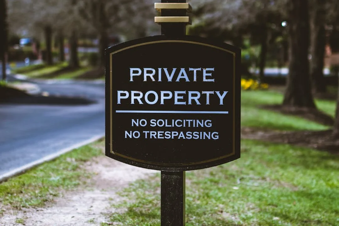 Close-up of a black private property sign with white lettering that reads 'PRIVATE PROPERTY', 'NO SOLICITING', and 'NO TRESPASSING' on a post beside a grassy path.