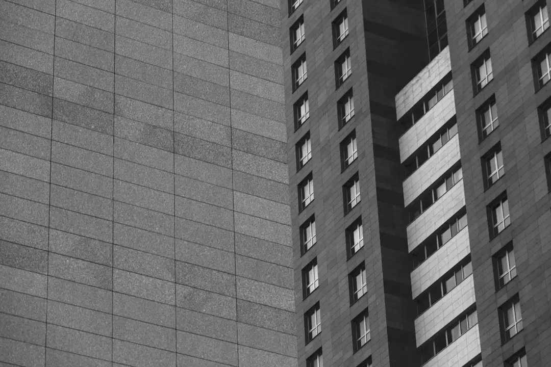 Black-and-white photo of tall apartment buildings with stacked windows, illustrating urban residential structures.