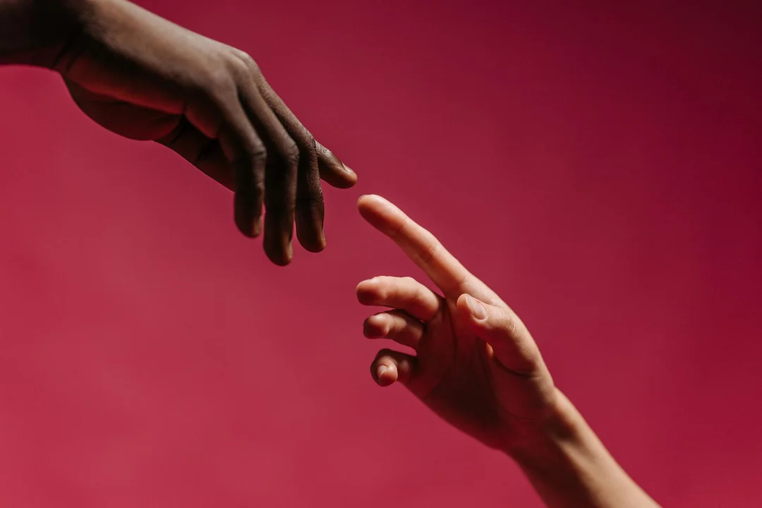 Two hands reaching toward each other against a red backdrop, symbolizing outreach and engagement in HOA communications.
