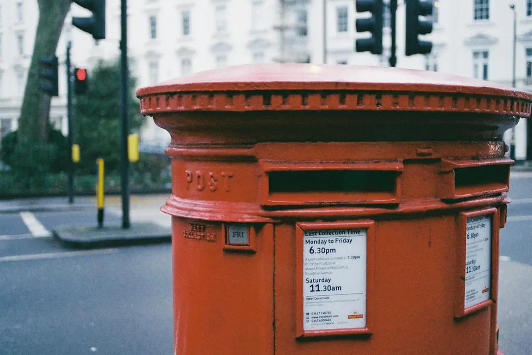 Red classic post box on a city street with a crosswalk and white buildings in the background.
