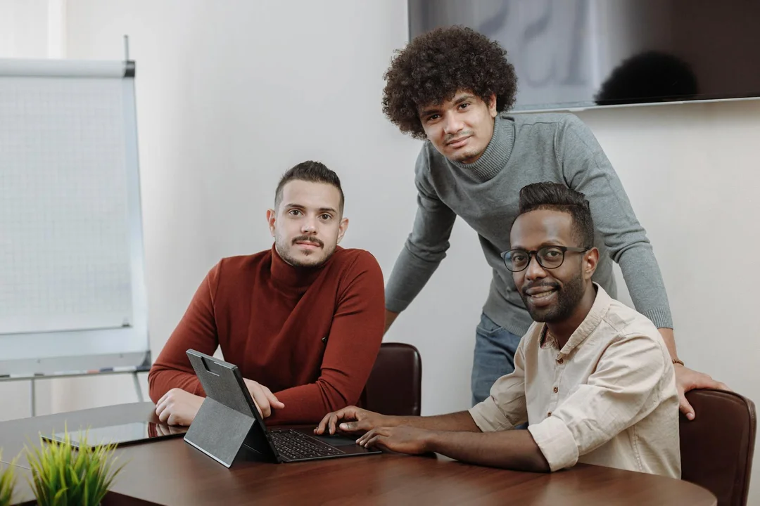 Three professionals collaborate around a conference table with a laptop and a flip chart, planning how to present reserve fund needs to homeowners.