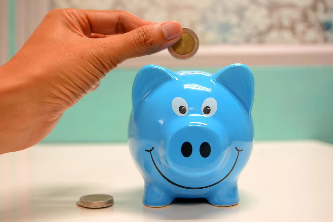 Blue piggy bank with a hand placing a coin into it, illustrating savings for HOA reserve funds.