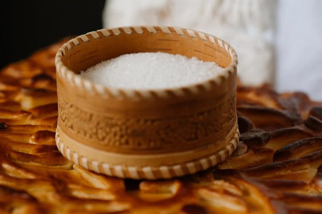 A wooden salt cellar filled with white salt sits on a rustic flatbread, symbolizing hospitality and provisioning.
