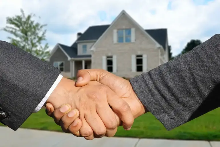 Two professionals shake hands in front of a suburban house, symbolizing HOA agreements and obligations.