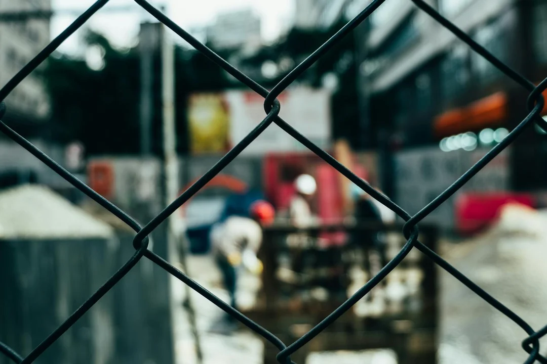 Close-up of a chain-link fence with a blurred construction site in the background.