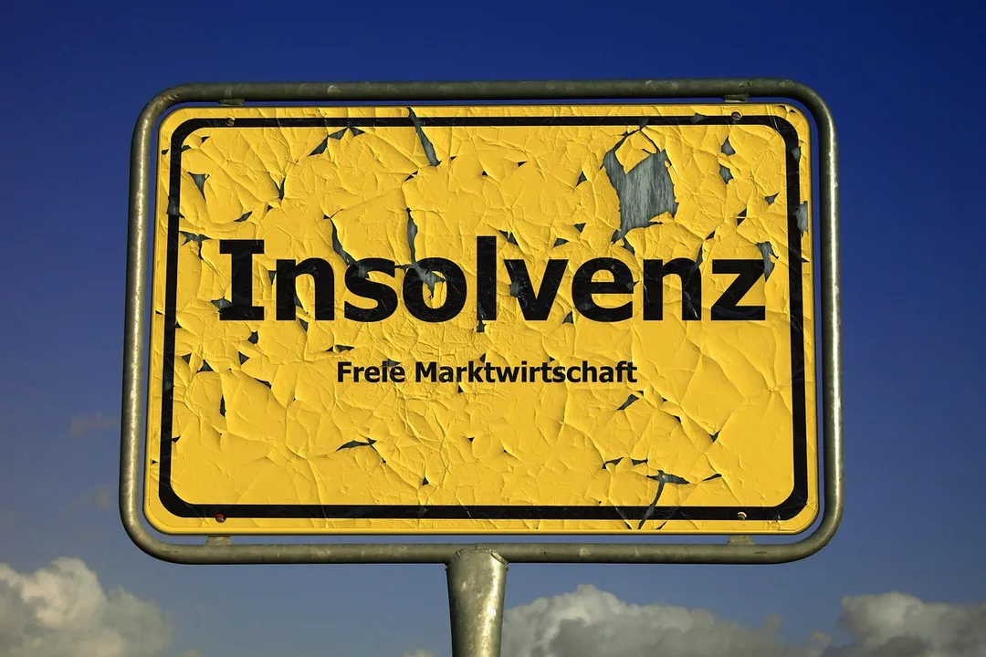 Weathered yellow sign with the word 'Insolvenz' (insolvency) printed on it, against a blue sky.