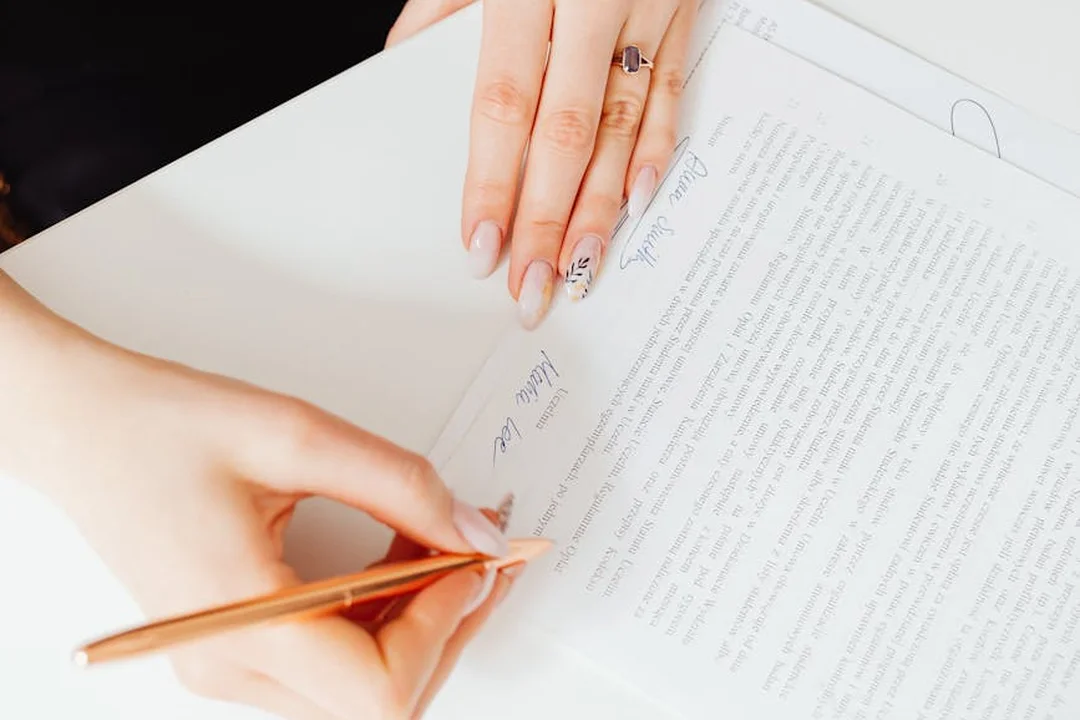 Close-up of hands signing a document with a pen over a stack of papers