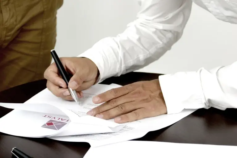 Close-up of hands signing documents at a desk with scattered papers, representing HOA paperwork