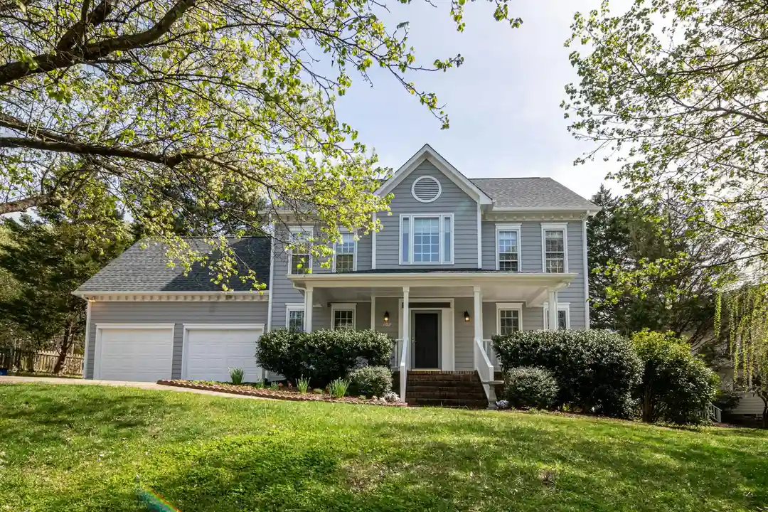 Front exterior of a two-story suburban single-family home with a manicured lawn, a driveway, and surrounding trees.