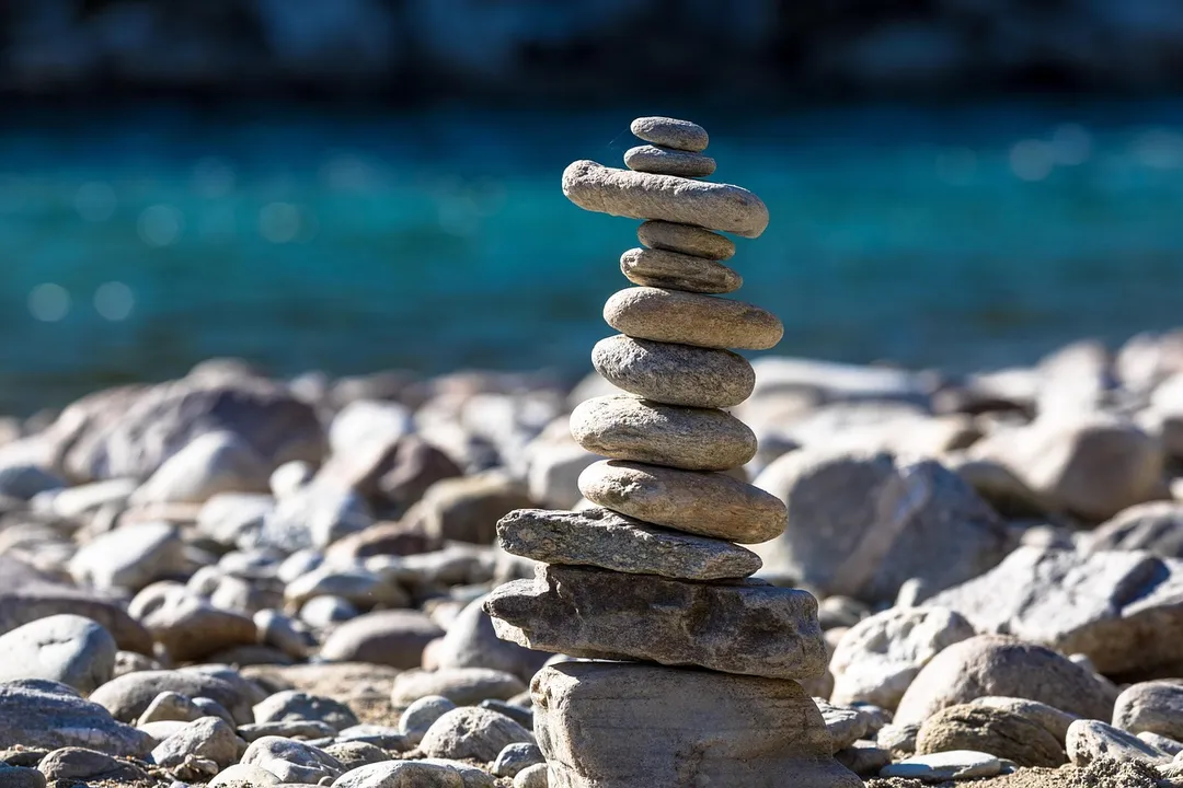 A balanced stack of smooth stones on a rocky shore with a blurred blue ocean in the background, symbolizing stability and careful governance.