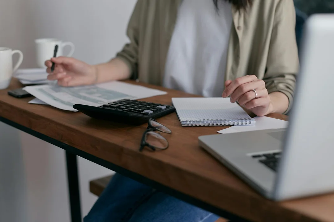 Person at a desk using a calculator and taking notes, with a laptop nearby, illustrating tax planning for HOA fees.
