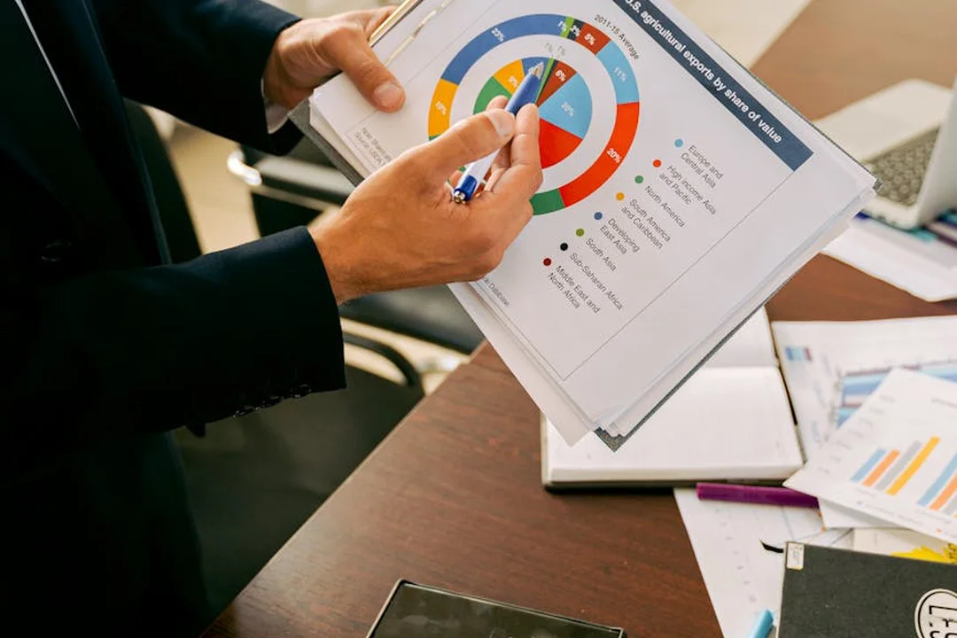 Close-up of hands in a dark suit marking financial documents with charts and graphs on a desk