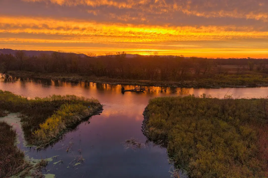 A marshy landscape at sunset with winding water channels and low-lying vegetation reflecting warm orange hues in the sky.