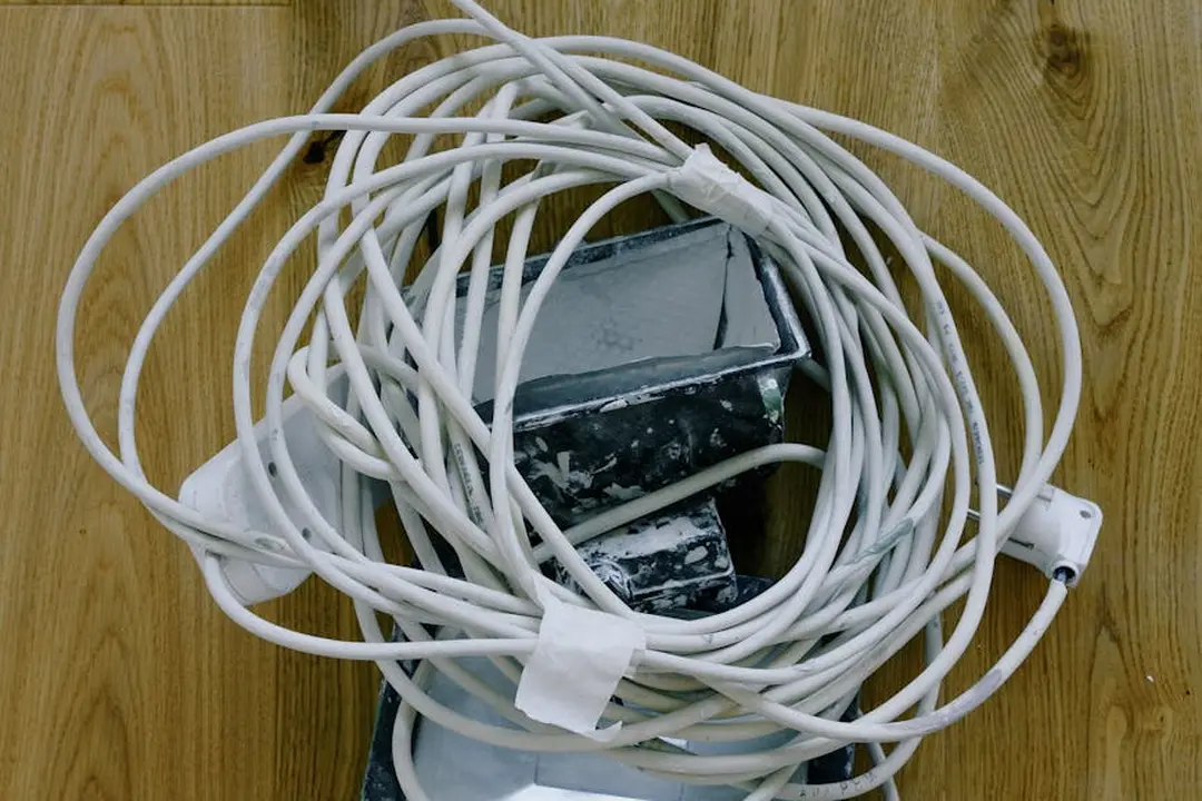 Tangled white electrical cords and a power adapter resting on a wooden floor.