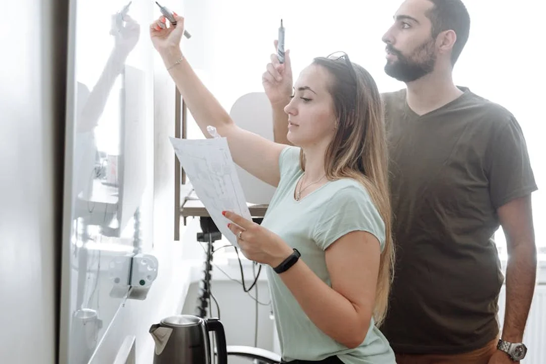 A man and a woman review documents and mark notes on a whiteboard during an HOA governance planning session.