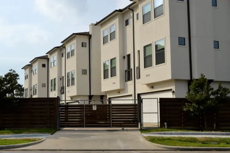 Row of modern townhouse units with a dark wooden fence and gated entrance.