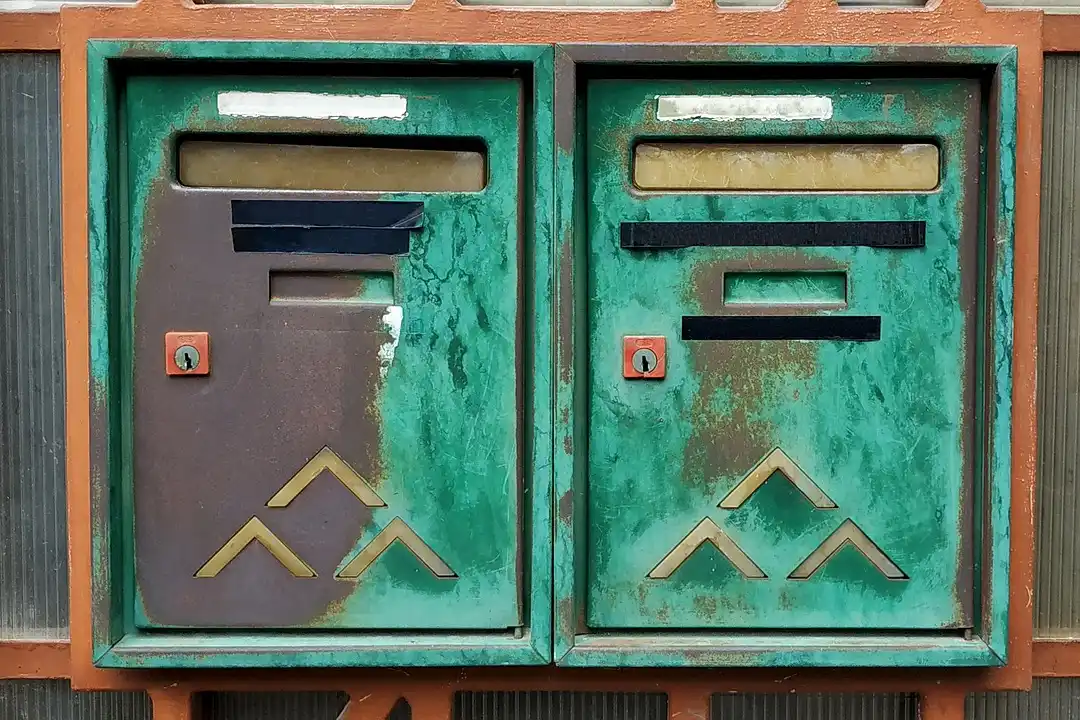 Two green metal mailboxes mounted on a wall, weathered and worn.