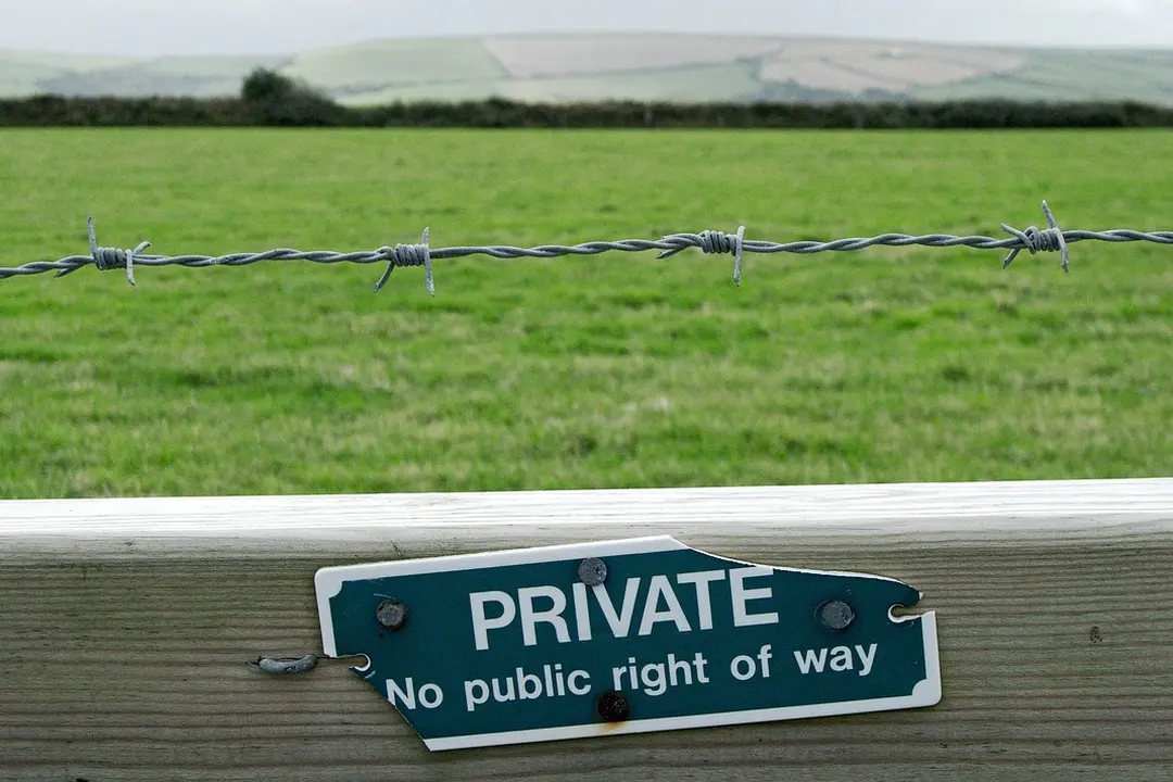 Green field behind a barbed-wire fence with a 'Private — No public right of way' sign on a wooden post