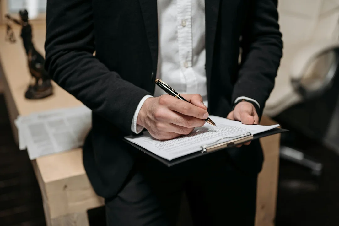 Professional in a suit writing on a clipboard, illustrating contract review, changes, and dispute-resolution planning in an office setting.
