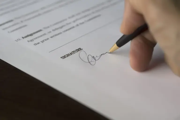 Close-up of a hand holding a pen and signing a document, with the word 'SIGNATURE' visible on the page.