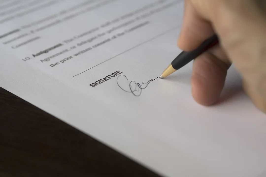 Close-up of a hand holding a pen and signing a document, with the word 'SIGNATURE' visible on the page.