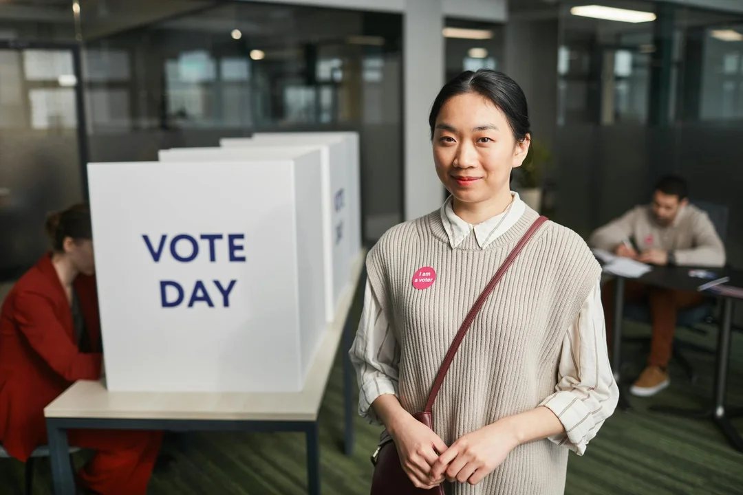 A woman stands near a voting box labeled 'VOTE DAY' at a polling station.